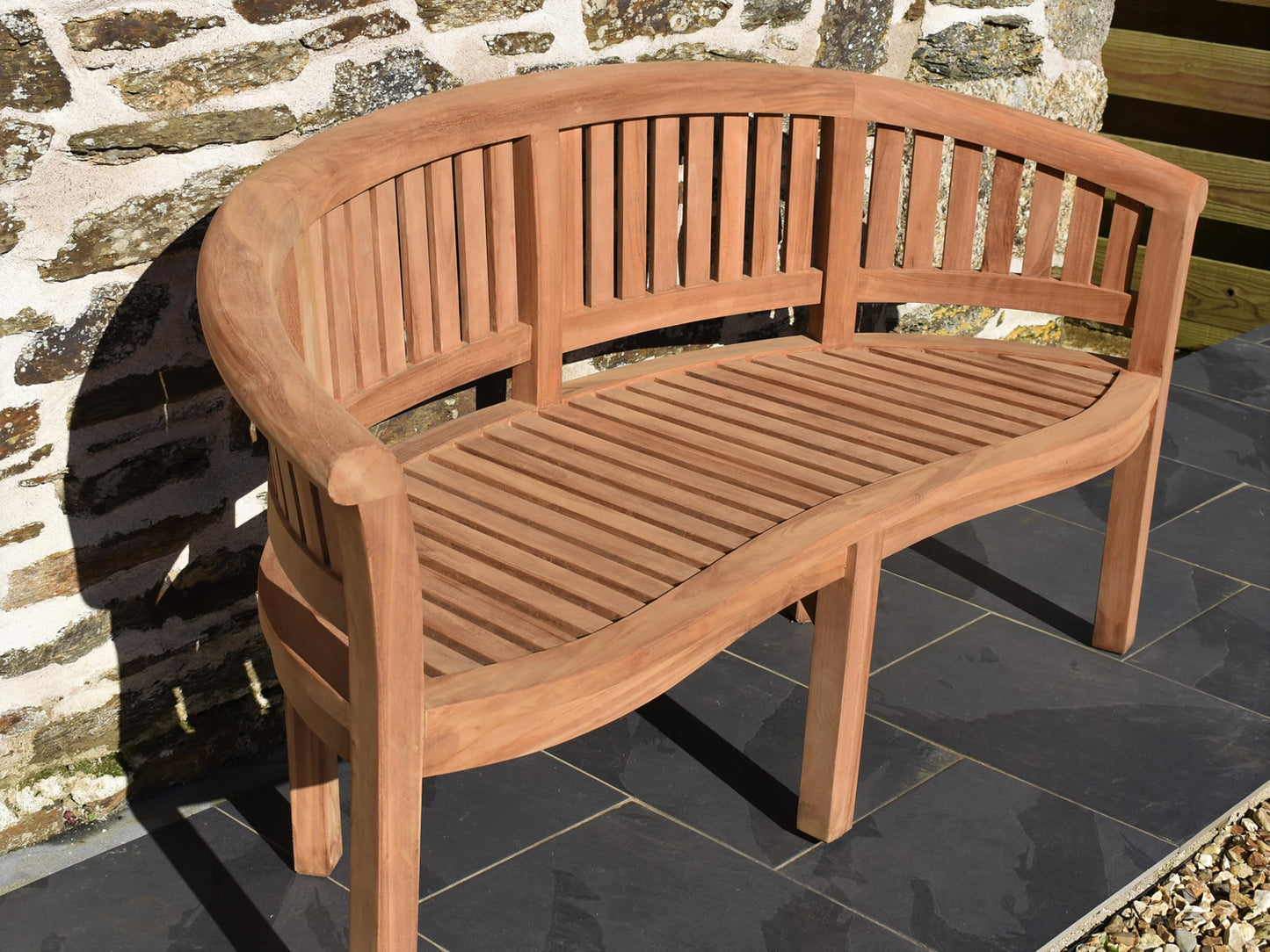 Classic teak garden banana bench on a patio, perfect for UK gardens