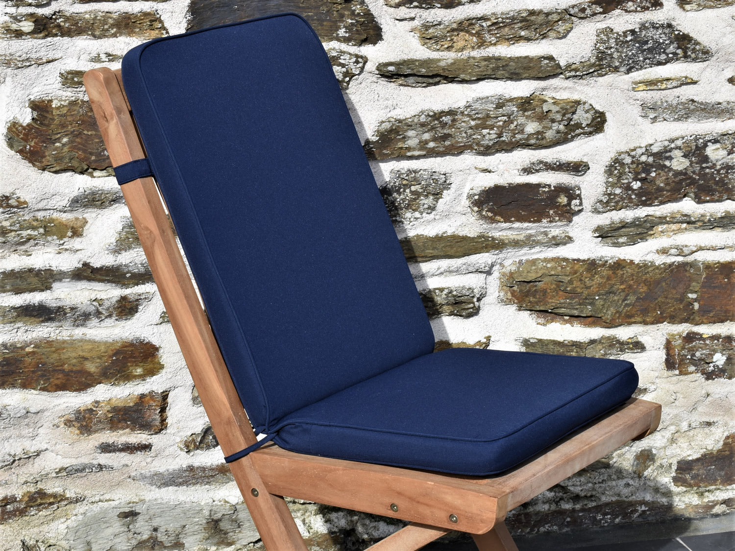 Close-up of dark blue fabric folding outdoor pad/back chair cushion, finished with matching fabric piping, ties and back strap