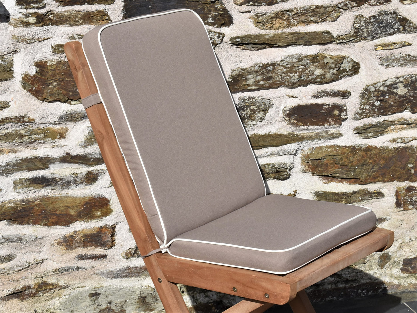 Close-up of luxury taupe colour folding seat pad and back outdoor cushion, finished with contrast white fabric piping and matching fabric ties and back strap 